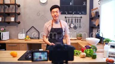 年轻的亚洲男人在厨房用<strong>相机录制</strong>视频。 微笑的亚洲男人在食品博客概念与水果和蔬菜
